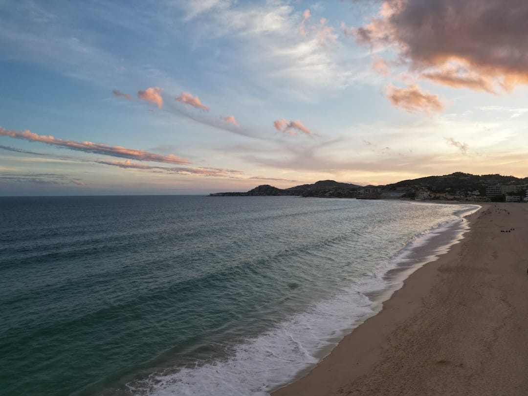 A happy, relaxed couple walks hand-in-hand at the water's edge on a beautiful Cabo beach, conveying a sense of safety, peace, and everyday enjoyment.
