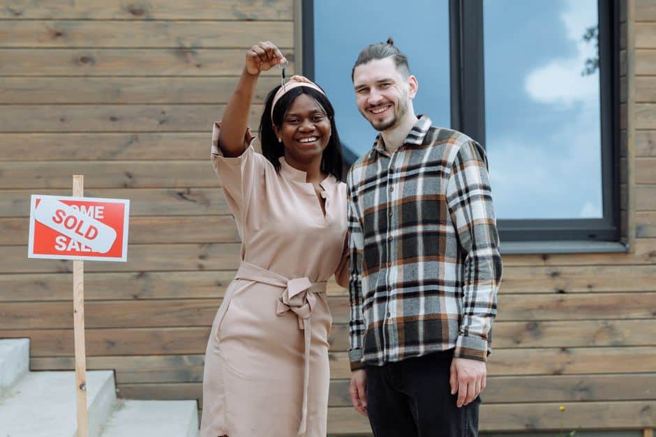 A smiling couple holds the keys to their new modern home with an ocean view, celebrating their successful property purchase in Mexico.