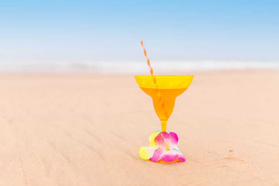 A colorful margarita cocktail rests on a balcony railing with the beautiful orange and pink hues of a Cabo sunset over the ocean in the background.
