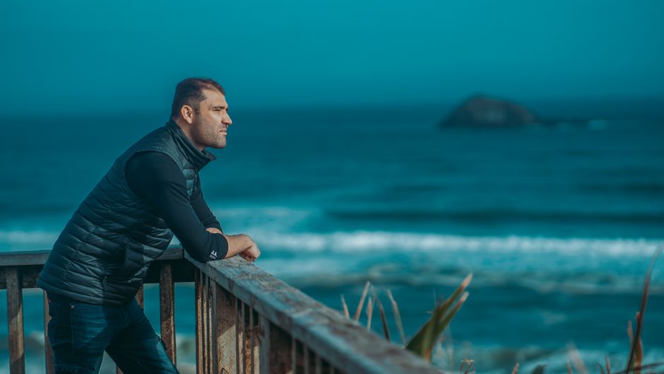 A man stands thoughtfully on the balcony of a modern luxury home, looking out at the ocean in Cabo, contemplating the realities of property ownership.