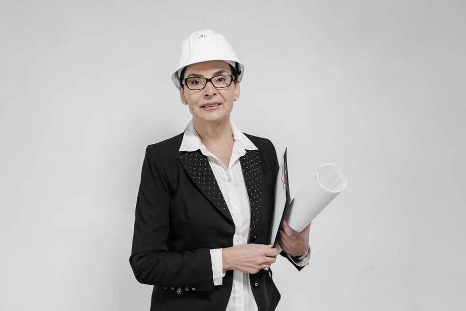 A professional and friendly realtor pointing to details on a blueprint while speaking with a client at a sunny home construction site in a tropical location.